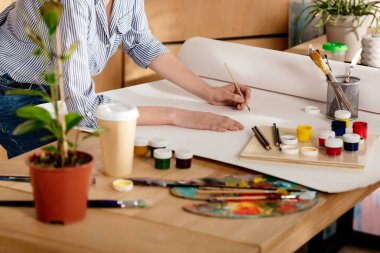 cropped shot of young female artist drawing on table in studio clipart