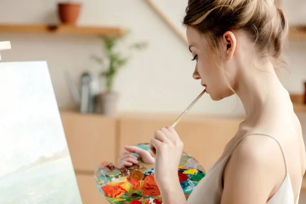艺术工作室中有吸引力的女画家的侧面观看调色板和画笔 — 图库照片