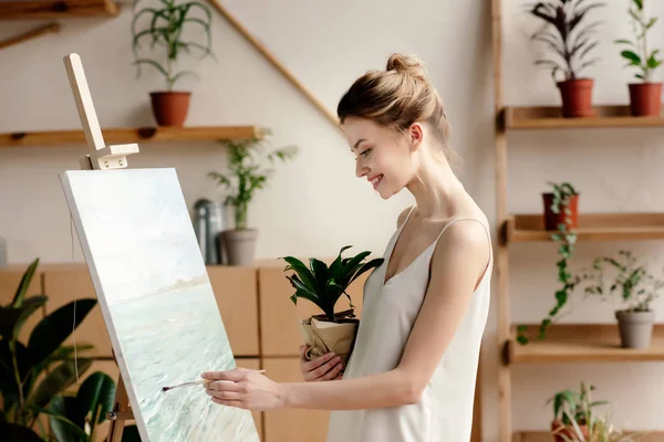 Zijaanzicht Van Glimlachen Van Jonge Vrouw Met Ingegoten Plant Schilderij — Stockfoto