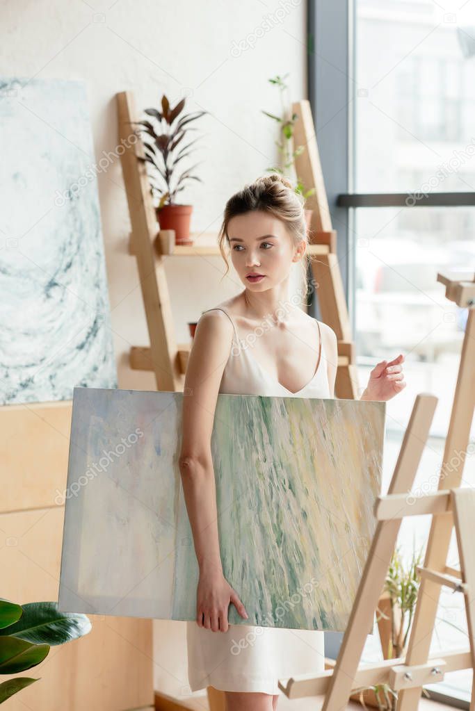 beautiful young woman holding picture and looking away in art studio 