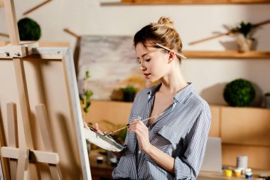 female artist with paintbrush behind ear drawing picture in studio clipart