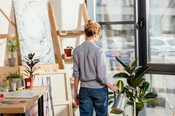 вид сзади на молодую художницу поливающую горшок завод в студии
