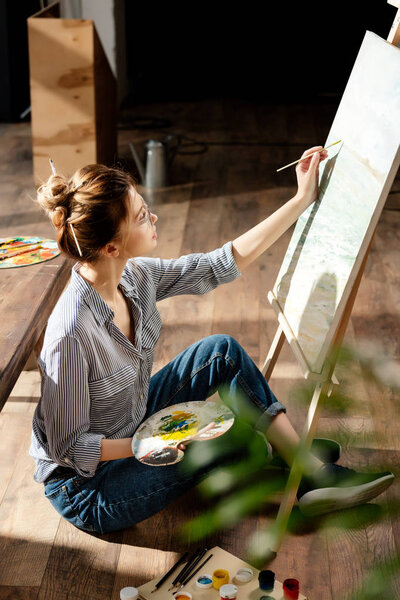 side view of stylish female artist in eyeglasses painting on easel