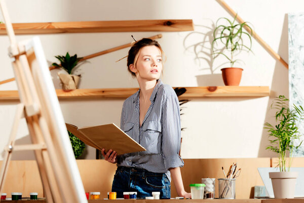 young attractive female artist holding book and looking away 