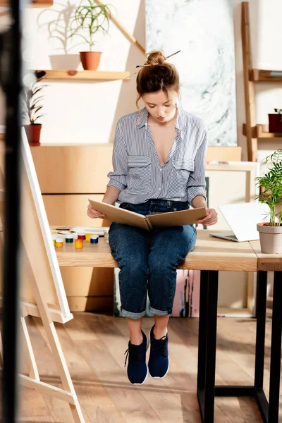 Giovane Artista Donna Che Legge Libro Seduto Sul Tavolo Con — Foto stock gratuita