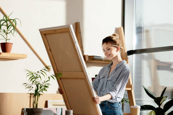  female artist with paintbrush behind ear smiling and looking at own picture 