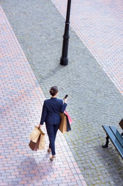 alışveriş torbaları ile yürüyüş ve smartphone kullanarak işkadını yüksek açılı görünüş