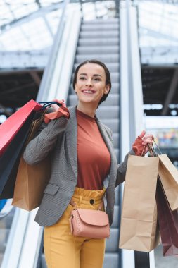 alışveriş torbaları ile yürüyen merdiven arka planda tutan çekici kadın