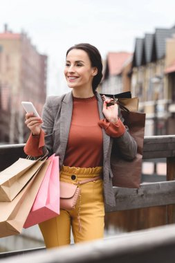 çekici kadın alışveriş torbaları ve köprü üstünde smartphone ile ayakta