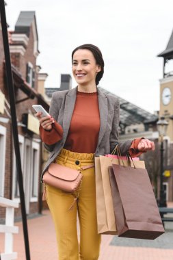 gülümseyen kadın alışveriş torbaları ve smartphone ile yürüme
