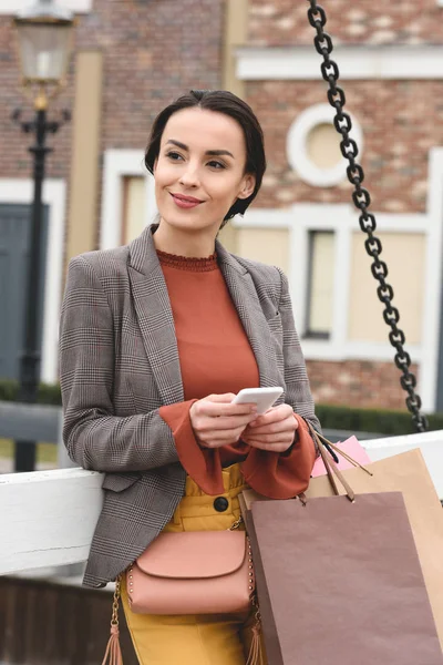 Ελκυστική Γυναίκα Κρατώντας Τσάντες Για Ψώνια Και Smartphone Και Ψάχνει — Δωρεάν Φωτογραφία