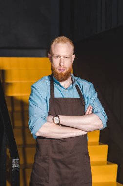 önlük ayakta çapraz kolları olan genç erkek barista portresi