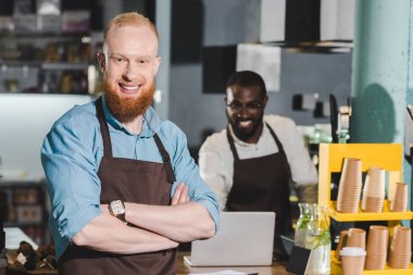 önlük erkek barista arkasında dizüstü kullanarak meslektaşım ile gülümseyen genç