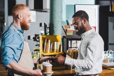 kredi kartıyla ödeme ve terminal ve kağıt bardak kahve ile erkek barista gülümseyen bir Afrikalı-Amerikalı adam