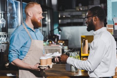 Sipariş ödeme ve erkek barista kağıt bardak kahve ile tutarak gülümseyen Afrikalı-Amerikalı adam 