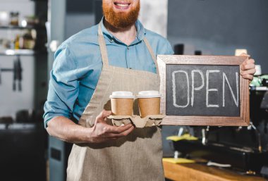 Kara tahta harflerle açık ile ve iki bardak kahve tutan genç erkek barista kırpılmış atış 
