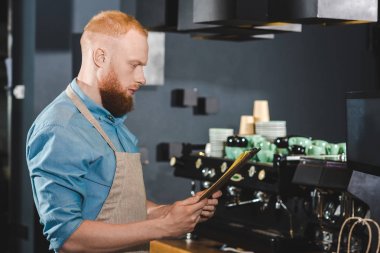genç erkek barista kahve dükkanı menüde bakarak yan görünüm 