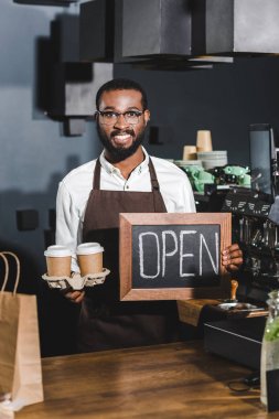 gözlük işareti açık ve tek kullanımlık kağıt bardak, kahve dükkanı kamerada gülümseyen tutan genç Afro-Amerikan barista