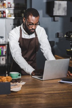 young african american barista using laptop while working in cafe clipart