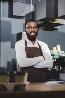 yakışıklı genç Afro-Amerikan barista çapraz kolları ile ayakta ve kamera kafede gülümseyen gözlük içinde