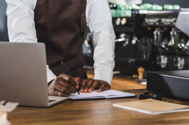 Not alma ve kahve dükkanında dizüstü kullanarak genç Afro-Amerikan barista kadeh kırpılmış
