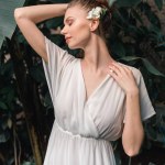 Attractive tender bride in white dress with flower in hair posing in tropical garden