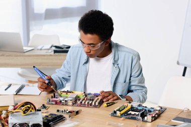 african american teenager soldering computer circuit with soldering iron at home clipart