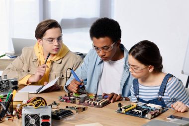multicultural teenagers soldering computer circuit with soldering iron at home clipart