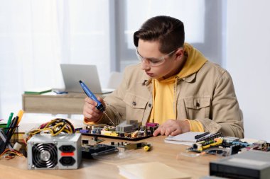 teen boy soldering computer motherboard with soldering iron at home clipart