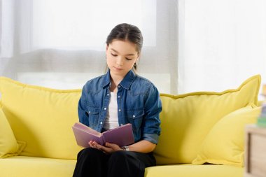Sarı koltukta oturan ve evde kitap okuma sevimli varoluş çocuk
