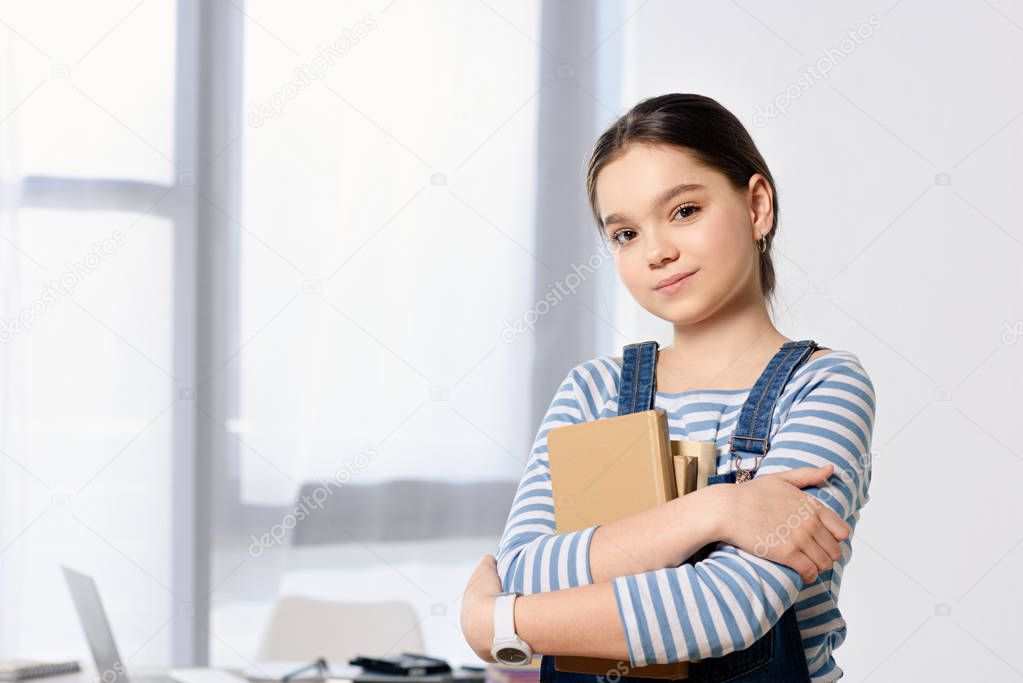 portrait of adorable preteen child standing with books at home