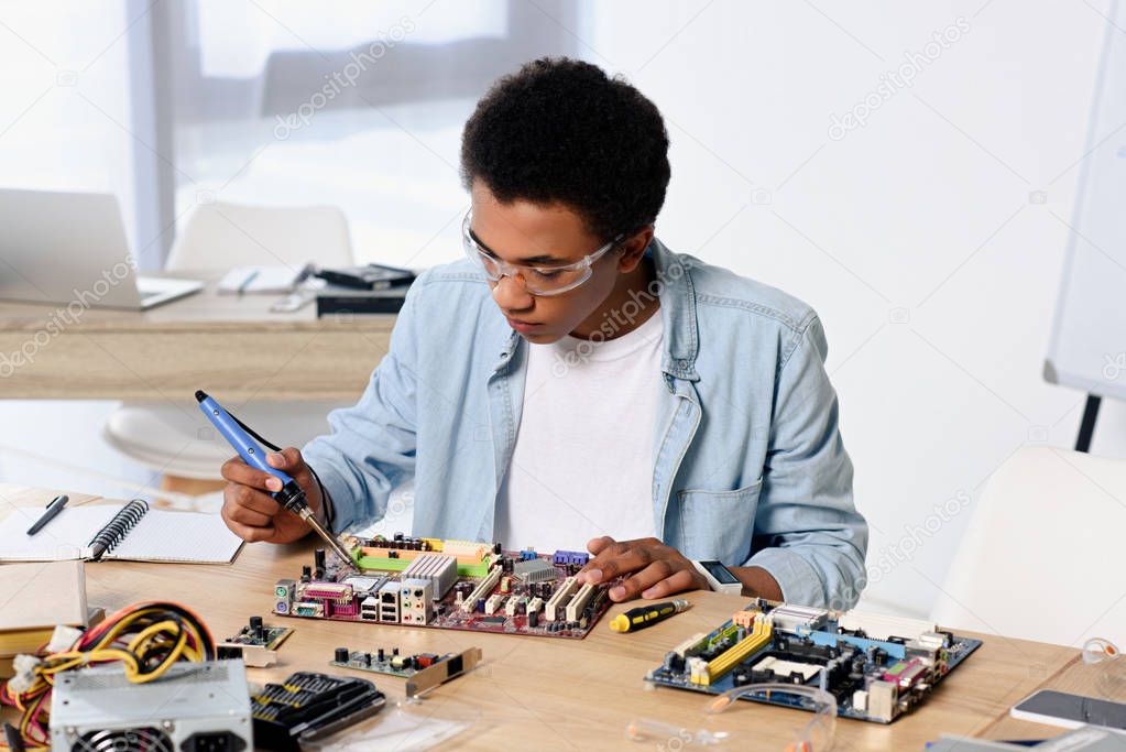 african american teenager soldering computer circuit with soldering iron at home