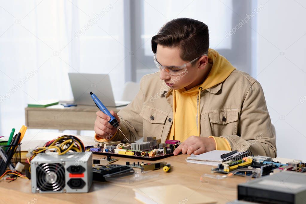 teen boy soldering computer motherboard with soldering iron at home