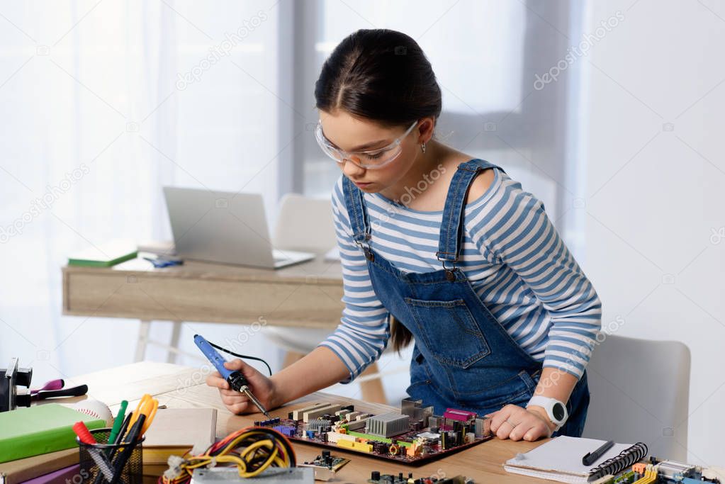 female teenager soldering computer motherboard with soldering iron at home