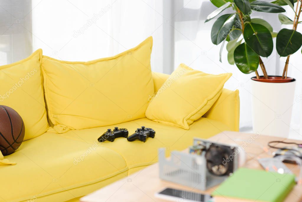 gamepads and basketball ball on yellow sofa at home