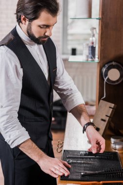 handsome young barber taking tools from rubber mat on workplace clipart