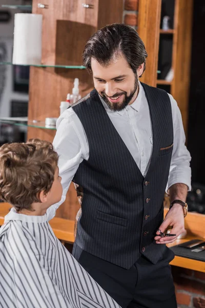 Guapo Feliz Peluquero Hablando Con Niño Pequeño Mientras Sentado Silla — Foto de stock gratis