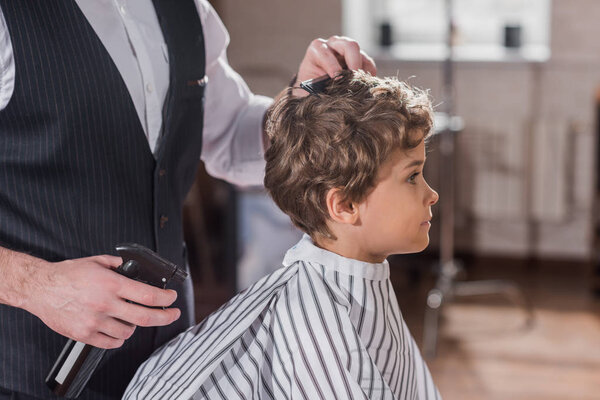 cropped shot of barber combing hair of little kid at kids barbershop