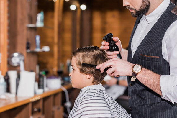 side view of barber combing and spraying hair of curly kid