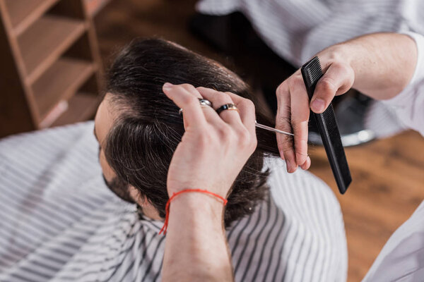 high angle view of barber cutting hair of customer with scissors