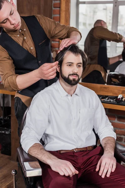 理发店的年轻理发师梳头发的顾客 — 图库照片