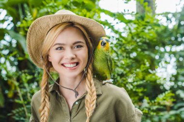happy young woman in safari suit with parrot on shoulder in jungle clipart