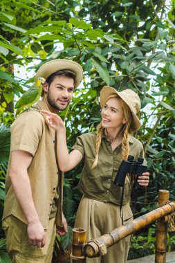 attractive young couple in safari suits with binoculars hiking together in rainforest clipart
