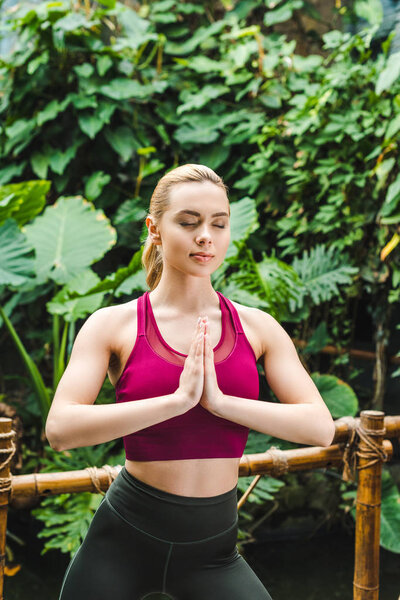 beautiful young woman practicing yoga in park and making namaste mudra