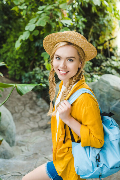 beautiful young woman in straw hat walking down stairs in park and looking at camera