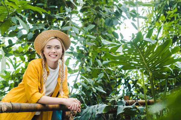 beautiful young woman in straw hat spending time in botanical garden