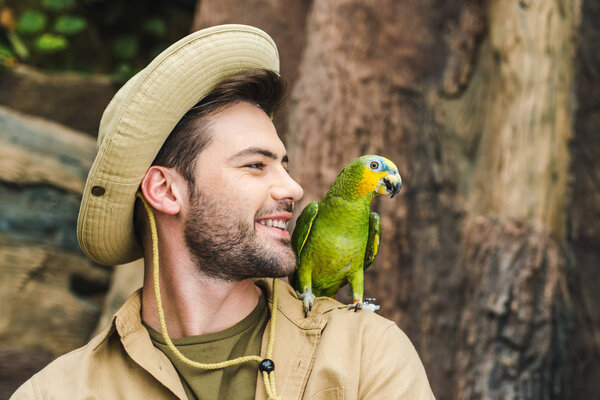 handsome young man with parrot on shoulder in jungle