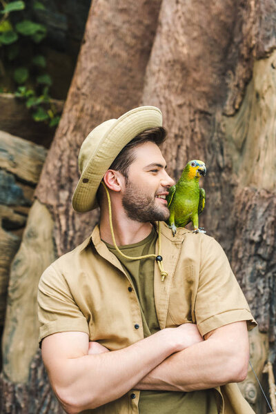 handsome young man with parrot on shoulder and crossed arms in jungle