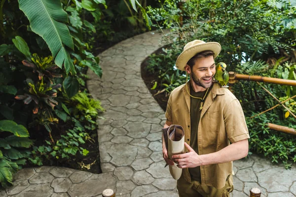 ジャングル公園にウォーキングの肩にオウムとハンサムな若い男 — ストック写真