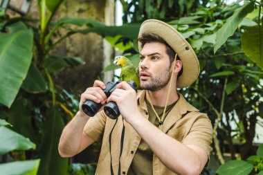 shocked young man with parrot on shoulder and binoculars in jungle clipart